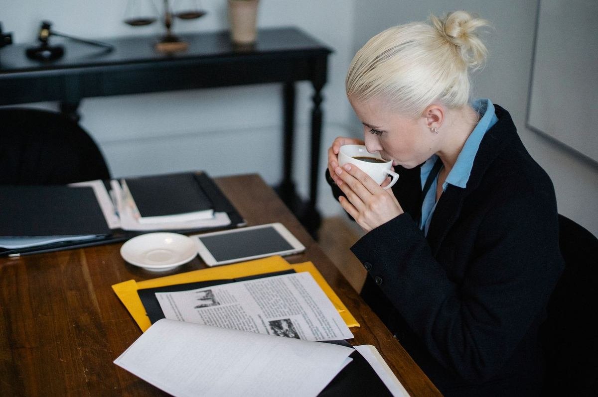 Femme buvant du café à un bureau avec des documents Femme buvant du café à un bureau avec des documents