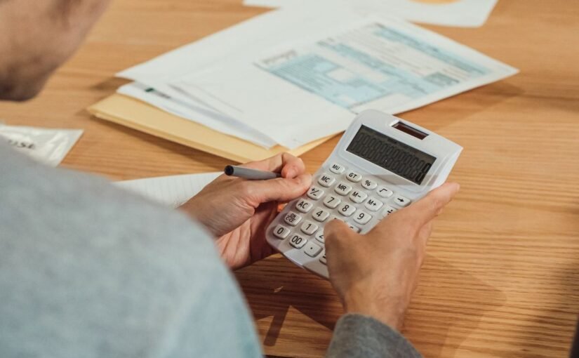 Homme utilisant une calculatrice et un stylo sur un bureau avec des documents