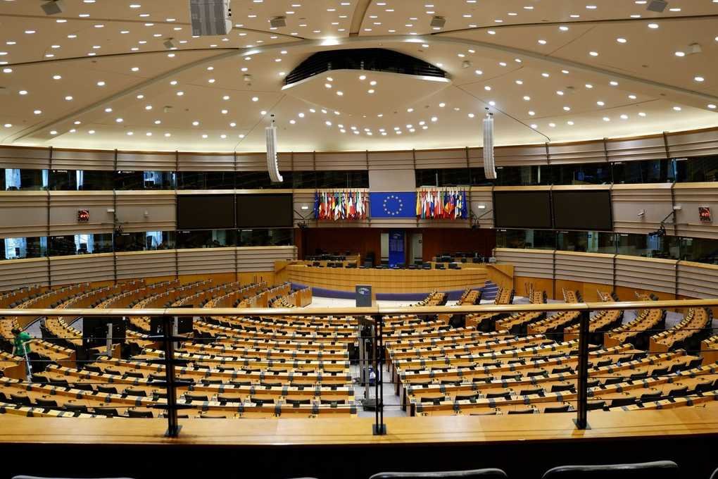 Salle de réunion vide avec des sièges en bois, un podium central et des drapeaux sur un écran