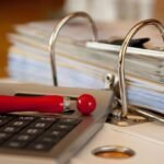 Calculatrice, stylo rouge et classeur à anneaux sur un bureau de travail administratif