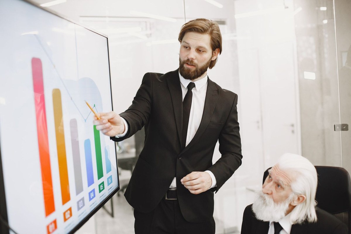 Présentation d'un graphique coloré à un collègue âgé dans un bureau moderne Présentation d'un graphique coloré à un collègue âgé dans un bureau moderne