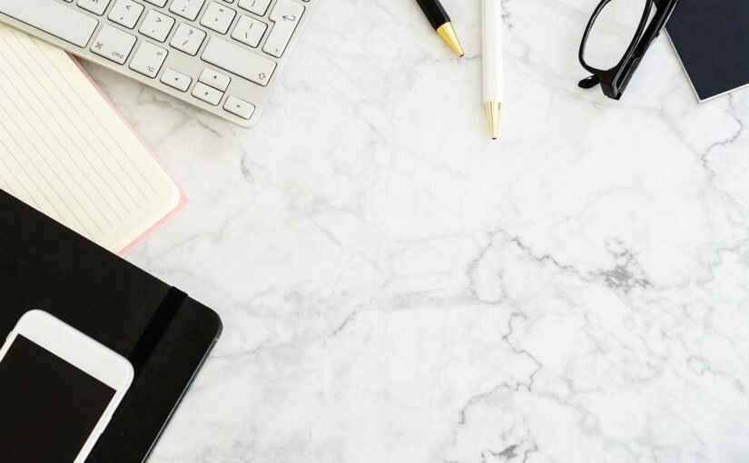 Clavier, notes, téléphone, ciseaux et stylos sur une surface marbrée