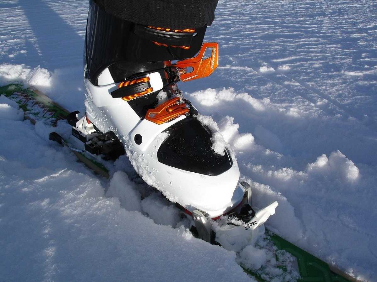 Botte de ski blanche et noire avec attaches orange sur pied posé sur neige