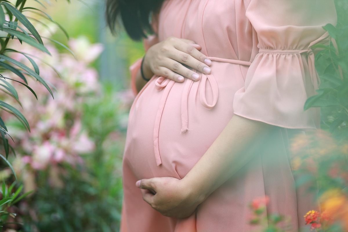 femme enceinte en robe rose tenant son ventre dans un jardin femme enceinte en robe rose tenant son ventre dans un jardin