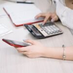 Femme manipulant un smartphone et une calculatrice sur une table de bureau