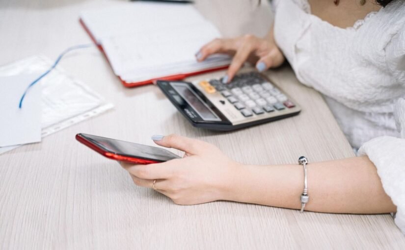Femme manipulant un smartphone et une calculatrice sur une table de bureau