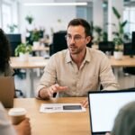 Quatre professionnels réunis autour d'une table de travail avec laptops et documents dans un bureau lumineux