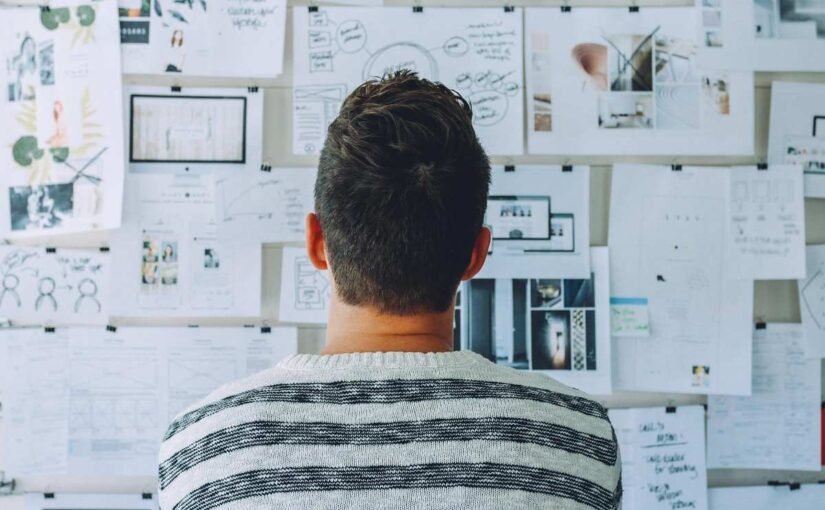 Homme observant un mur couvert de documents, schémas et wireframes de projet