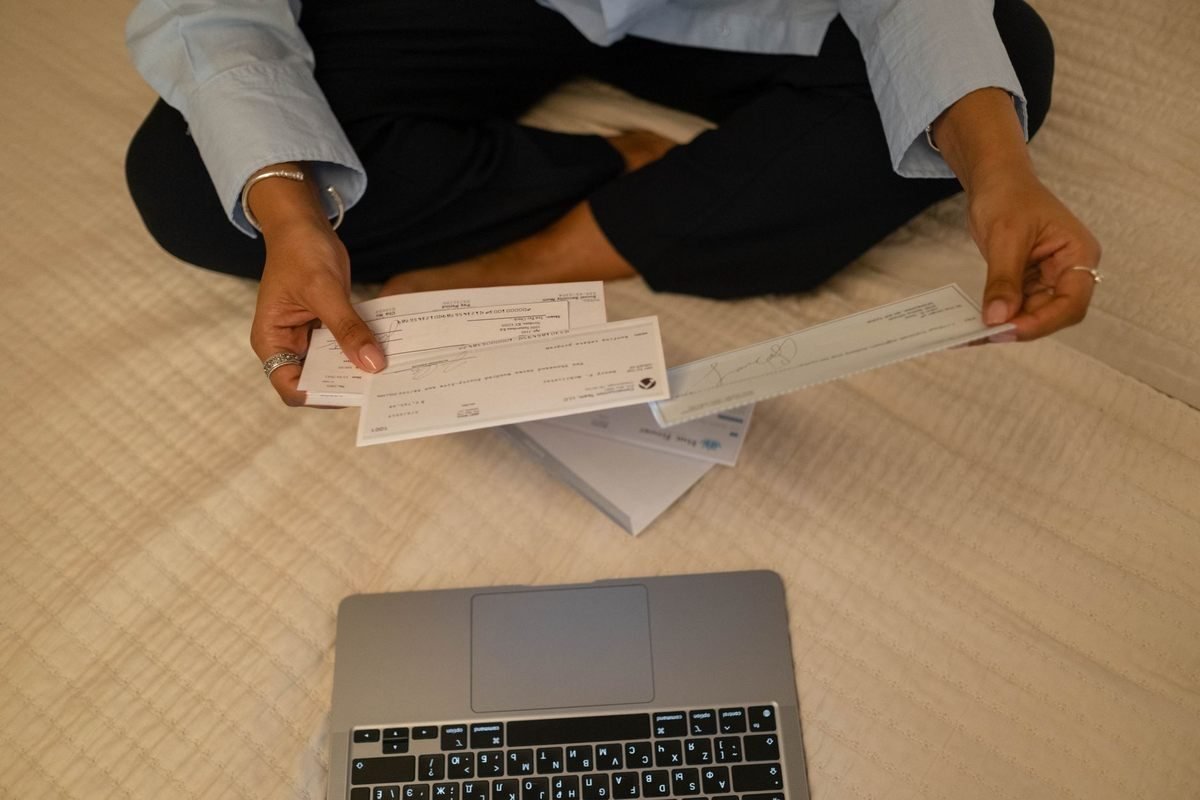 Une personne examine des chèques près d'un ordinateur sur un lit