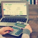 Person utilisant un ordinateur portable et une calculatrice sur une table en bois