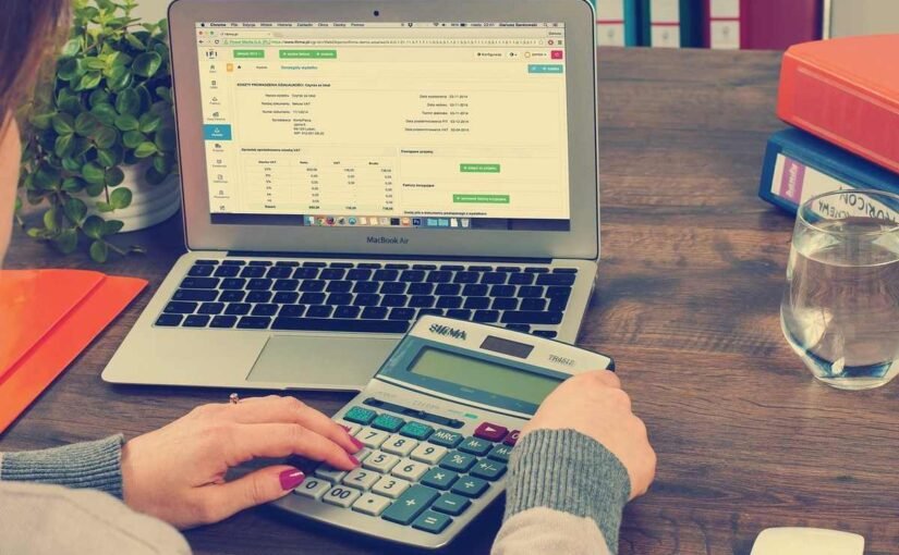 Person utilisant un ordinateur portable et une calculatrice sur une table en bois