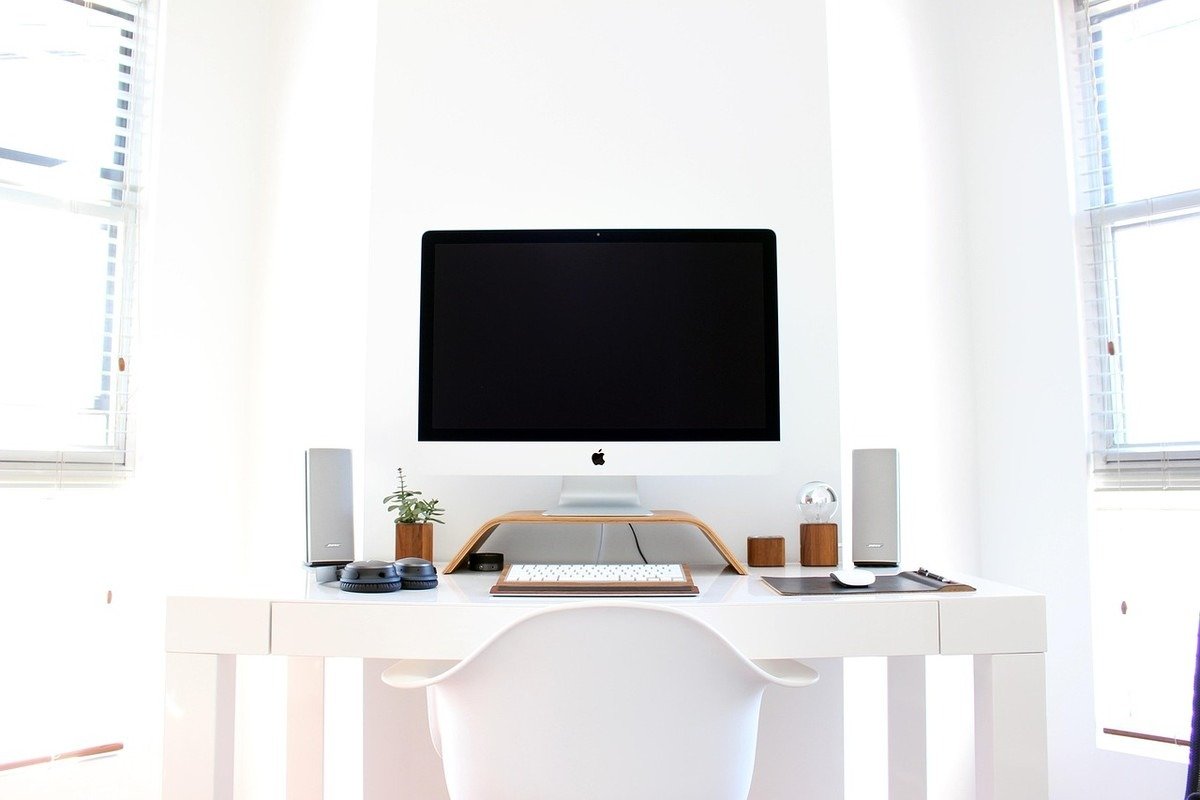 Bureau épuré blanc avec moniteur noir, chaise et objets de décoration, fenêtres latérales