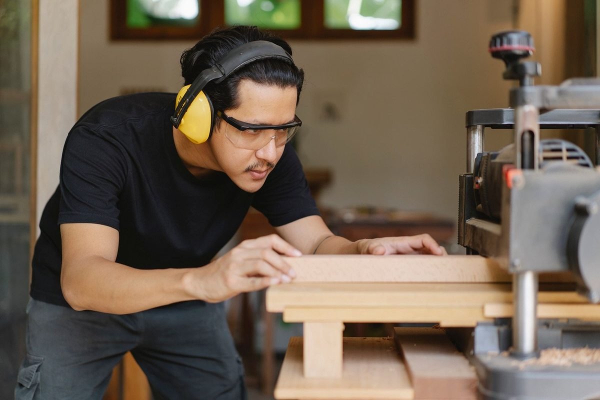 Homme en noir utilise une scie à table dans un atelier, portant protections auditives et visuelles Homme en noir utilise une scie à table dans un atelier, portant protections auditives et visuelles
