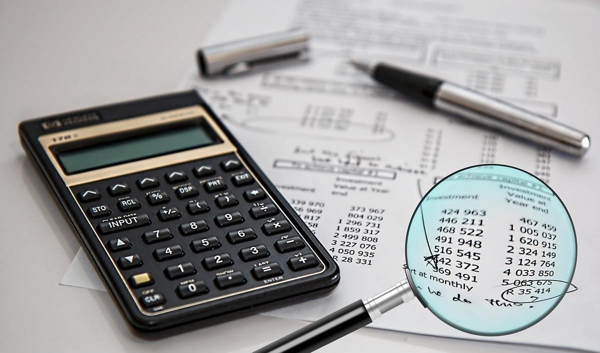 Une calculatrice, un stylo, du papier et une loupe sur un bureau