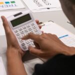 Une personne manipule une calculatrice sur une table avec des documents et graphiques colorés