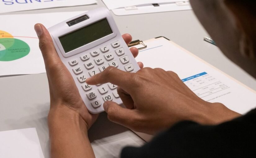 Une personne manipule une calculatrice sur une table avec des documents et graphiques colorés
