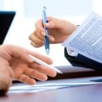Des mains tiennent des stylos et des papiers sur une table