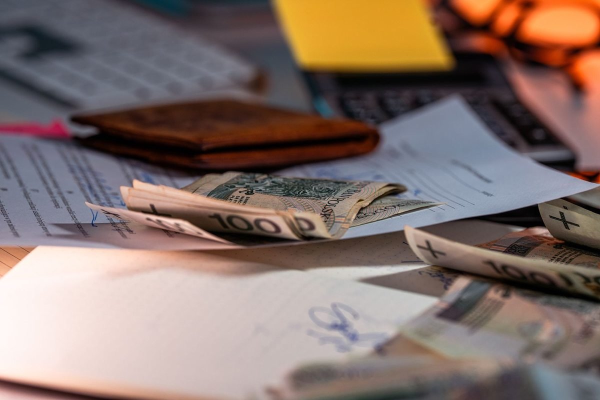 Billets de 100 dollars éparpillés sur une table avec un portefeuille, des papiers et un clavier Billets de 100 dollars éparpillés sur une table avec un portefeuille, des papiers et un clavier